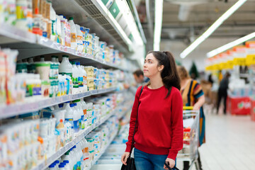A young pretty woman looking at the display cases with dairy products in the supermarket...