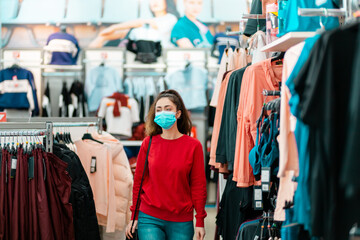 Antiviral protection in public places. A young pretty woman in a medical mask choosing clothes in a store. The concept of shopping during a viral pandemic