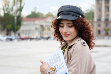 Young woman in leather hat holding newspaper on city square