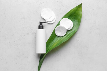 Clean cotton pads, cosmetic bottle and palm leaf on light background