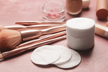 Clean cotton pads, decorative cosmetics and brushes on color background, closeup