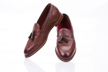 Footwear Ideas. Pair of Traditional Formal Stylish Brown Pebble Grain Tassel Loafer Shoes Together In Line Against White Surface.