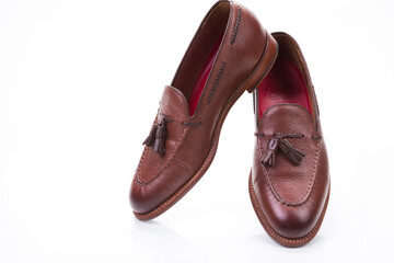Footwear Ideas. Pair of Traditional Formal Stylish Brown Pebble Grain Tassel Loafer Shoes Together In Line Against White Surface.
