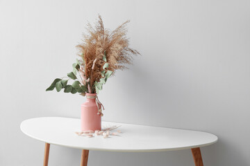 Vase with beautiful bouquet of dried flowers on table near light wall