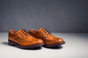 Male Footwear Ideas. Pair of Full Broggued Tan Leather Oxfords Broggued Shoes Against Gray  Background.