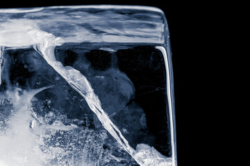 A large rectangle of clear ice with cracks, against the dark background. Block of clear pure frozen ice with air bubbles, isolated on black background.