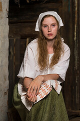 Lovely Portrait of Tranquil Caucasian Redhaired Girl in Rustic Style Dress Posing in Old Village House Near the Stove.