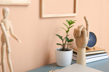 Wooden hand and houseplant on color table near wall