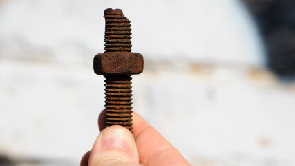 old rusty bolt, iron rod with screw threads, in hand. Rusted mechanical components. holding threaded bolt and nut. dismantling concept, difficult to unscrew, non-removable. isolated on light, close-up