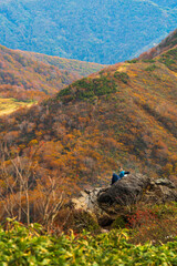 群馬県・谷川岳　天神尾根　大岩で休む登山者【Climbers taking a break while looking at the autumn leaves of the mountain】