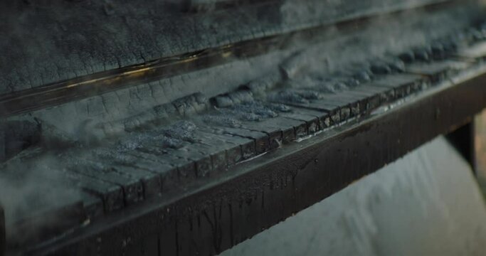 Piano burn and smoke. Footage of piano smoke. Black piano with smoke. Abandoned classic wooden piano with broken body frame and keys is slowly smoking after being put out of fire and flaming. 