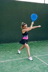 Woman playing paddle tennis, hitting the ball forehand, coming off the wall. 