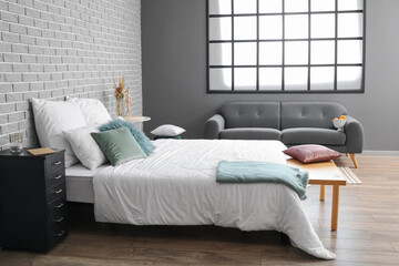 Interior of modern room with big comfortable bed and grey sofa