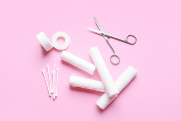 Cotton buds, medical plaster, surgical scissors and bandage rolls on color background