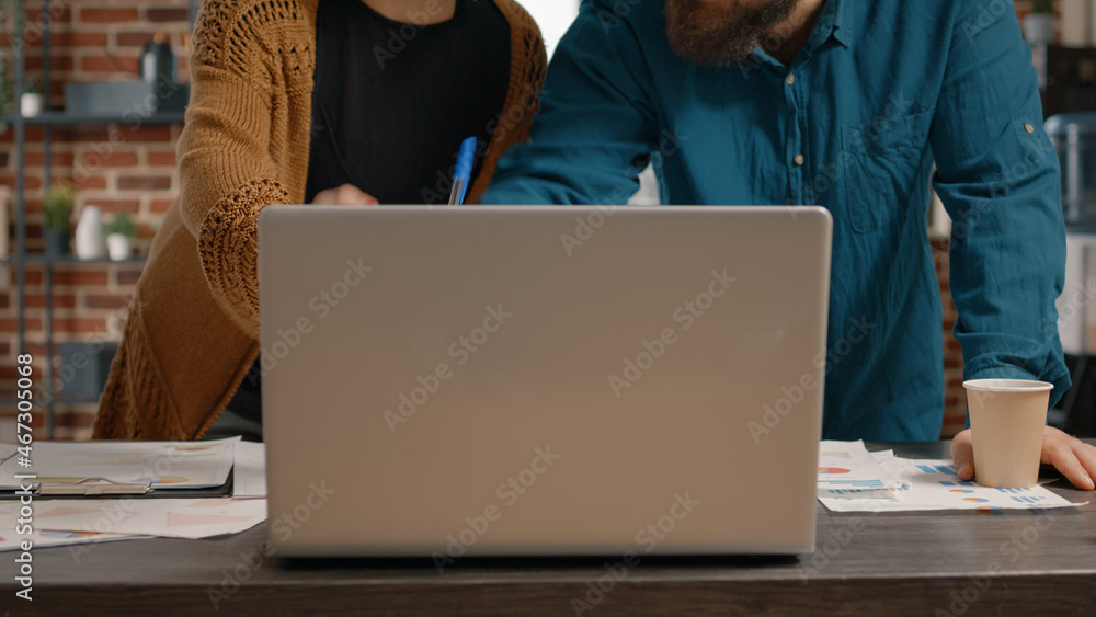 Poster workmates having discussion about business project, using laptop and papers with data charts to desi