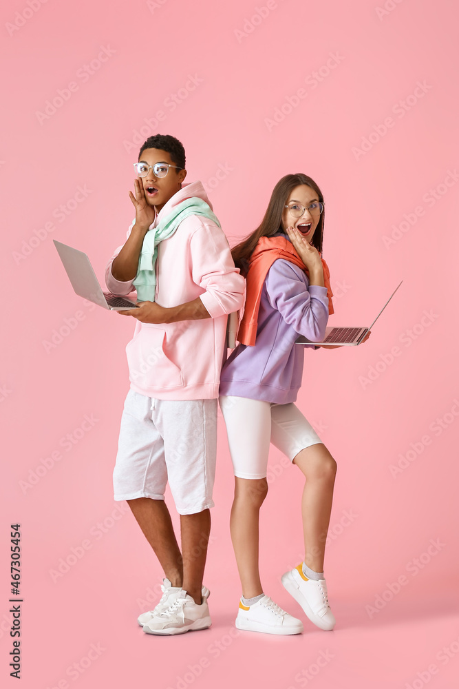 Canvas Prints Surprised young couple in hoodies with laptops on pink background