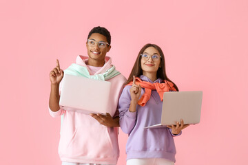 Stylish young couple in hoodies with laptops pointing at something on pink background