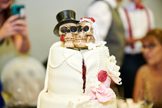 White wedding cake with a skull topper and red roses, the bride and groom in the form of a skeleton