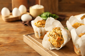 Board with tasty spinach muffins on wooden background, closeup