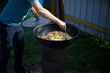 A man is stirring food cooked pilaf outdoors in a cauldron on an open fire , Asian cuisine