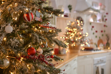 Festive fir tree branches with shiny red and white baubles, balls,snowy red berries, xmas ornaments on the background of beautiful blurred christmas kitchen, golden bokeh.Christmas background
