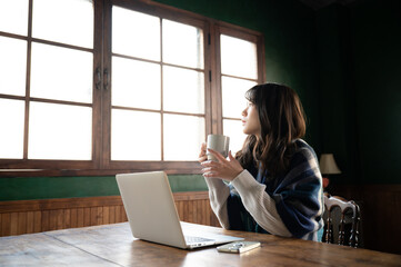 An Asian (Japanese) woman stares at the window while holding a cup of coffee wide angle
