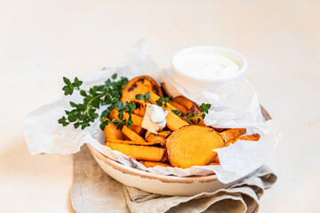 Healthy homemade baked sweet potato wedges with cream dip sauce and herbs on concrete background. Healthy snack.