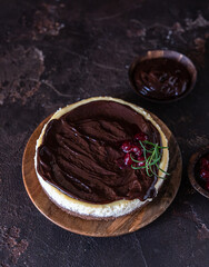 Creamy cheesecake with chocolate sauce and cherry decorated with rosemary on dark concrete background.