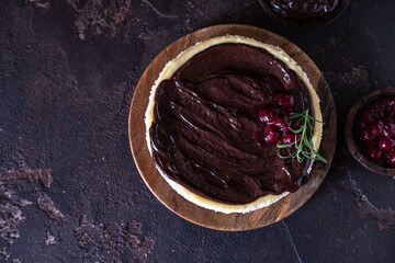 Creamy cheesecake with chocolate sauce and cherry decorated with rosemary on dark concrete background.