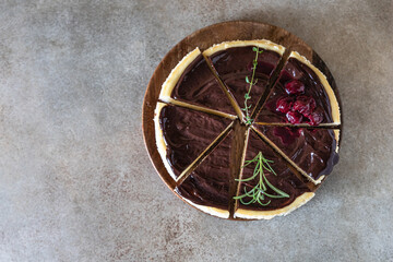 Fototapeta na wymiar Classic creamy cheesecake with chocolate ganache, cherries and rosemary on concrete background. Popular festive dessert. Top view.
