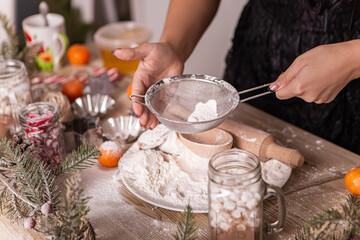 Kitchen rolling pin and wooden spoon appliances utensils flour sieve woman cook present culinary dinner tangerines, New Year evening, Christmas decorated home. Greeting congratulating holiday
 - Powered by Adobe