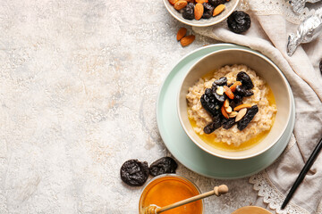 Bowl with delicious oatmeal, prunes and almond nuts on light table