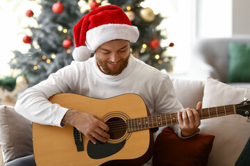 Young man in Santa hat playing guitar at home on Christmas eve