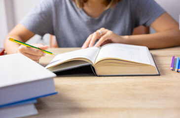 Top view and selective focus shot of woman who is reading textbook on table with stacks of many books as foreground shows education concept of hard studying and learning for gaining knowledge.