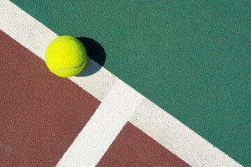 Yellow tennis ball lying on line of the red and green court. Flat lay view. Space for text