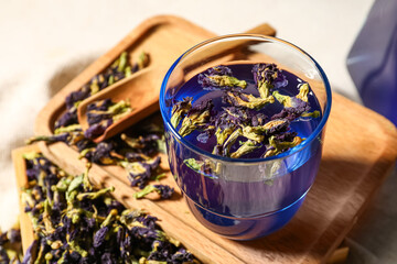 Wooden board with glass of blue tea and dried flowers on table
