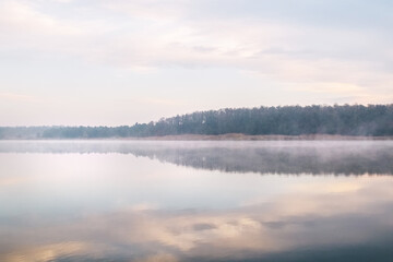 Background. Mountain lake in the fog. Magic morning. Fog spreads beautifully over the water surface. The trees are almost invisible. Clouds and sky are reflected from the surface