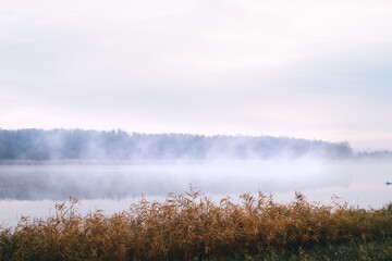 Background. Mountain lake in the fog. Magic morning. Fog spreads beautifully over the water surface. The trees are almost invisible. Clouds and sky are reflected from the surface