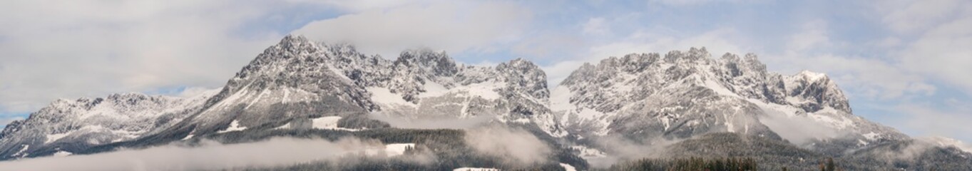 Fototapeta na wymiar Wilder Kaiser in Tirol Österreich mit ersten Schnee im Jahr umhüllt von Wolken und Nebelschwaden Panorama