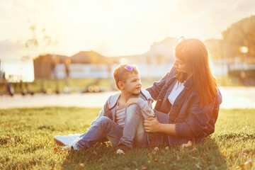 A young mother is resting with her son on the lawn in the park. Copy space. The concept of family activity