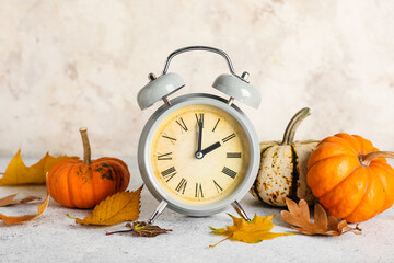 Alarm clock and autumn leaves with pumpkins on grunge background. Daylight saving time end