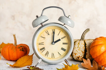 Alarm clock and autumn leaves with pumpkins on grunge background. Daylight saving time end