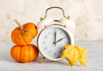 Alarm clock and autumn leaves with pumpkins on grunge background. Daylight saving time end
