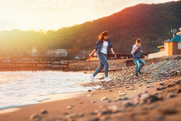 A young mother and her son playing together on the beach. In the background is the sea and sunset. The concept of a happy childhood