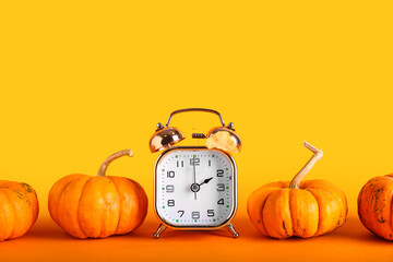 Alarm clock and pumpkins on color background. Daylight saving time end - Powered by Adobe