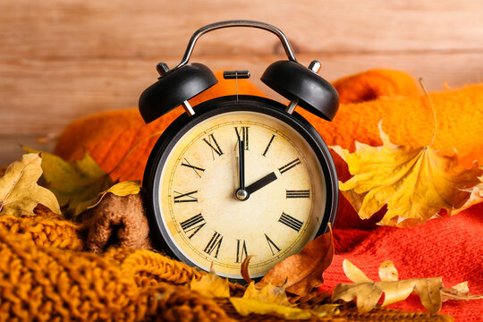 Alarm clock and autumn leaves with clothes on wooden background. Daylight saving time end