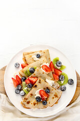 Sweet crepes with berries and cream on white wooden background.