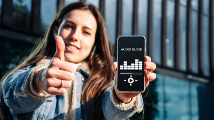 Audio tour online app on digital mobile smartphone. Happy young student woman holding phone...