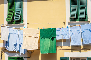 Group of towels and bathrobes hanging outside the window on a clothesline to dry in the sun. Tellaro village, Liguria, Italy, southern Europe.