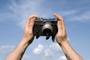Male hands holding retro film camera against blue sky
